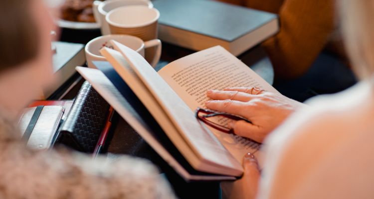 Depicts a close up of people's hands on books at a cafe.