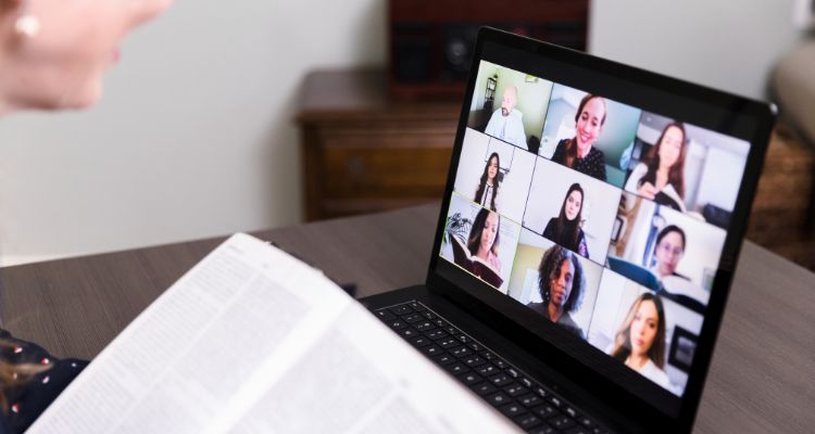 Depicts someone holding a book in front of a computer with people on a virtual call.