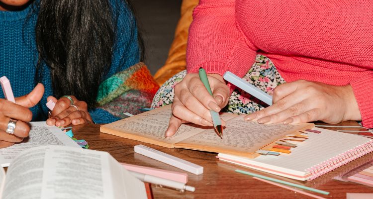 Depicts two people's hands annotating books with pens and highlighters.