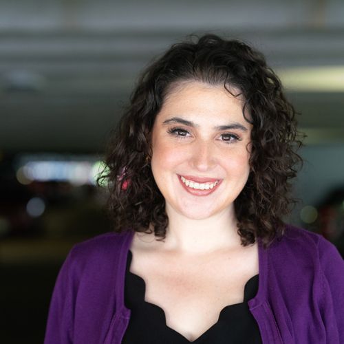 Author Lauren Magaziner, a light skinned woman with dark curly hair smiling sweetly to the camera.