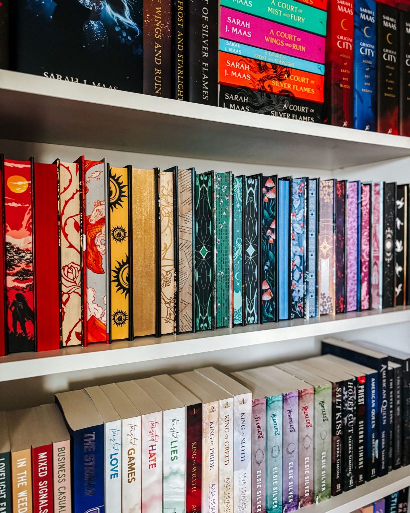 A close up of Makenna's bookshelves. The first shelf is mostly obscured, but features Sarah J. Maas's ACOTAR series, the central shelf features a collection of hardcover books with their intricately decorated pages facing the camera.