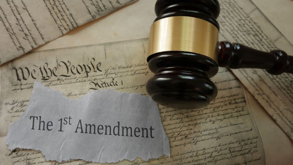 Gavel on a U.S. Constitution background with "The 1st Amendment" on torn paper.