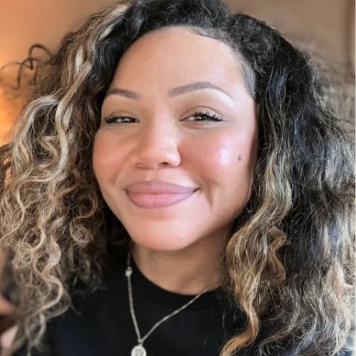 Paranormal romance author Britney S. Lewis, a Black woman with curly hair, smiles sweetly to the camera.