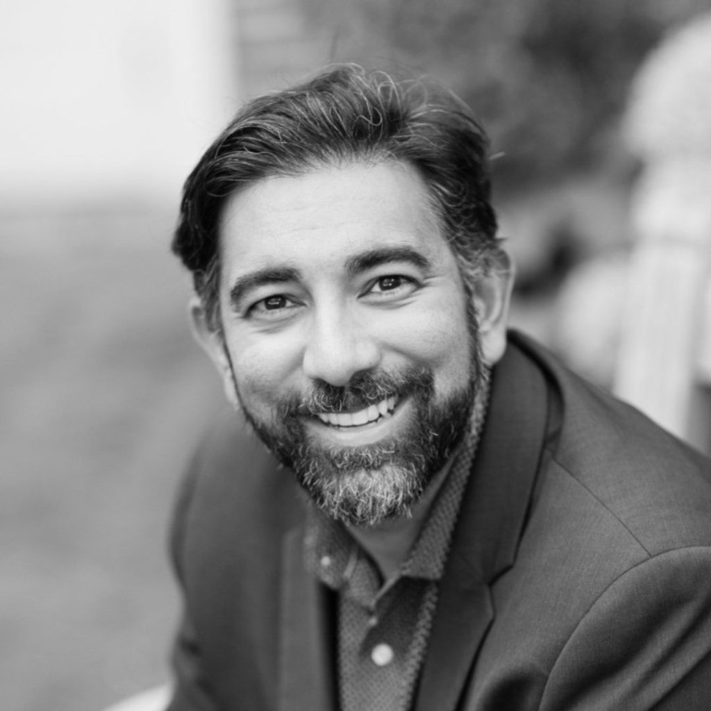 Dr. Bidhan Parmar wears a suit with a button-up shirt underneath and smiles. He has short, slicked-back hair and short facial hair.