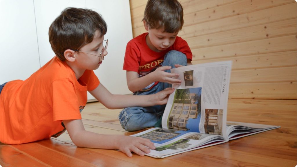 Two children on the floor, one older and one younger, reading a book together.
