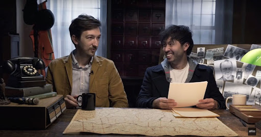 Still from Buzzfeed Unsolved depicting Ryan Bergara and Shane Madej sitting at a desk with various historical-looking items.