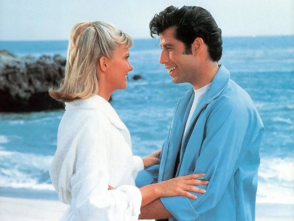Movie still from Grease. Characters Sandy and Danny stare lovingly into each other's eyes on a beach.