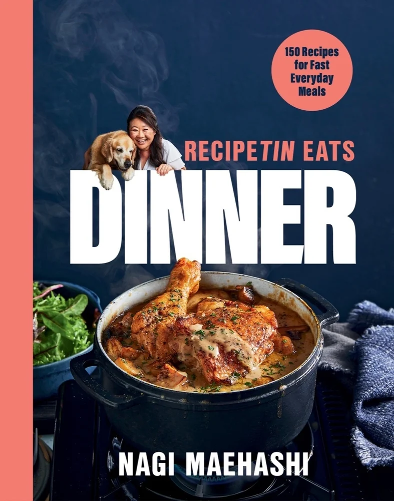 Dinner by Nagi Maehashi book cover, depicting chicken stew in a blue pot with a bowl of spinach next to it. The background is dark blue while the title is in white, bold text and other features are in pink.