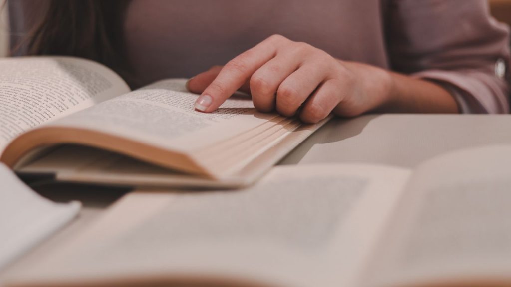 A woman's finger pointing to the page of an open book.