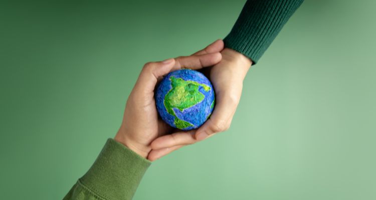 A green background, with two hands coming to hold a small paper globe in the middle. One is wearing a dark green shirt, and the other is wearing a light green shirt.