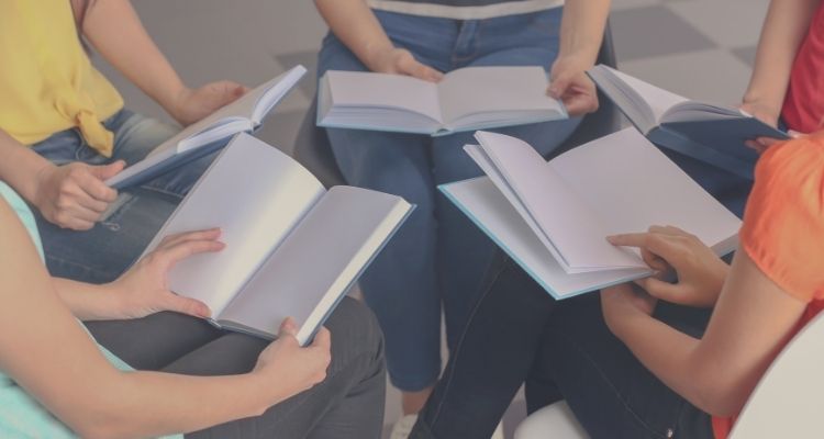 Depicts a circle of young peoples' hands all with books in them.