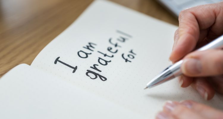 Depicts a journal page titles "I am grateful for..." with a hand holding a pen.