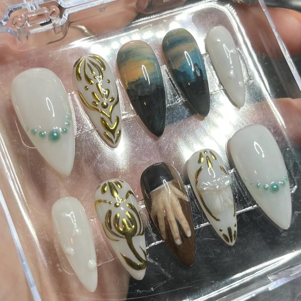 Set of 10 press-on nails in a clear plastic container. Two nails make up a landscape, and one of them features a man walking, resembling a scene from the 2005 adaptation of Pride and Prejudice. Another nail has a hand on it, also resembling a scene from the 2005 adaptation. The remaining nails have a white background. Some have gold accents, while others have white or teal pearls.