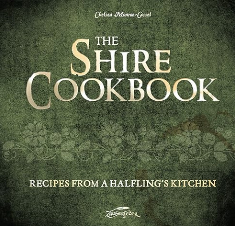 Cover of The Shire Cookbook: Recipes from a Halfling’s Kitchen by Chelsea Monroe-Cassel. The design features a rustic green textured background with floral patterns and elegant gold and white lettering.