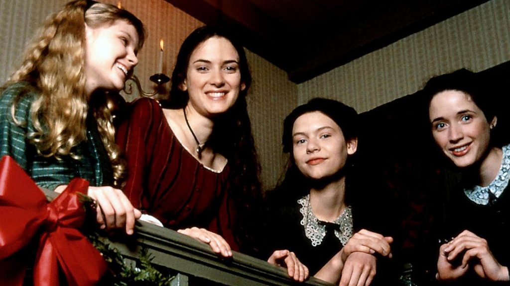 Movie still from Gillian Anderson's 1994 adaptation of 'Little Women'. Image depicting four young girls smiling from an upstairs landing, holding onto a banister covered in Christmas ribbon and garland.