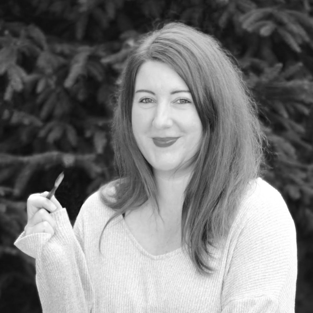 Photo of Martina Stuhlberger. Stuhlberger smiles at the camera with a pen in hand, pictured in black and white.