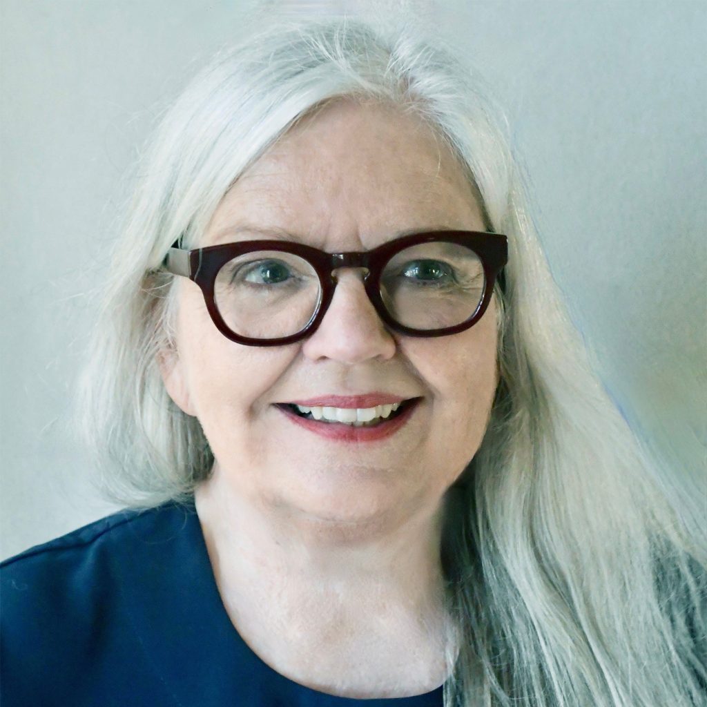 Antoinette Portis, a smiling light-skinned woman with long, straight white hair, wearing a navy blue blouse and brown glasses, posing against a white background.