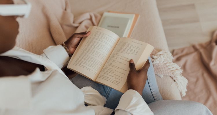 Image depicts a woman sitting on a couch and reading a book.