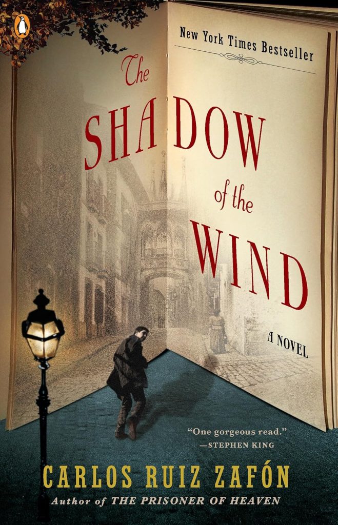 The Shadow of the Wind by Carlos Ruiz Zafón book cover. Depicts a corner of an opened book with a city street illustrated in the corner. A man walks toward the street.
