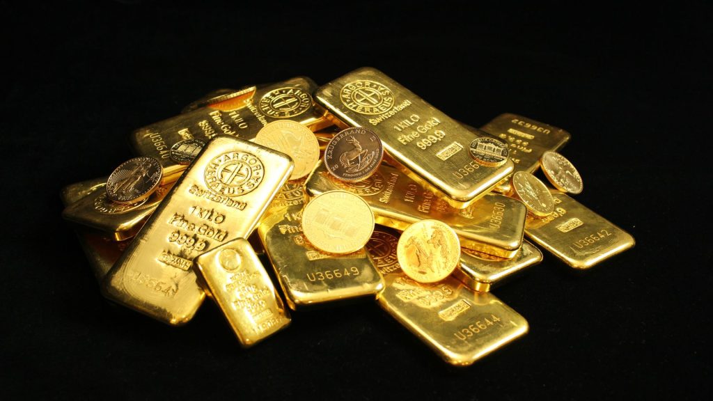 A pile of gold bars and coins engraved with the words "fine gold" on a black background.