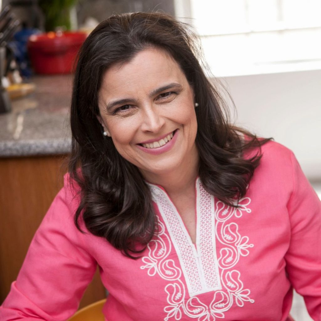 Isabel Vincent wearing a long-sleeved pink shirt with white embroidery in floral shapes around the v-neck collar and small white pearl earrings and smiling. She has fair skin and shoulder-length dark brown hair.
