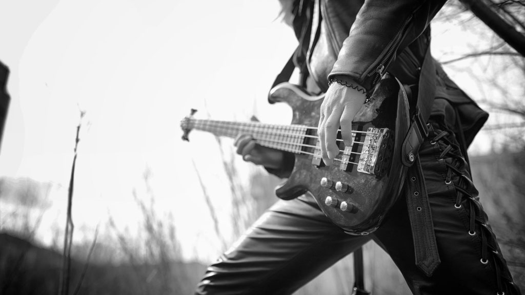 A person wearing a leather jacket and leather pants plays a guitar in a forest.