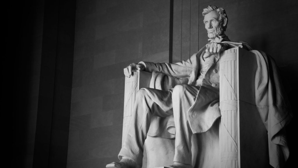 The Lincoln Memorial in Washington D.C. A large white monument of Abraham Lincoln sitting in a chair with a stoic facial expression.