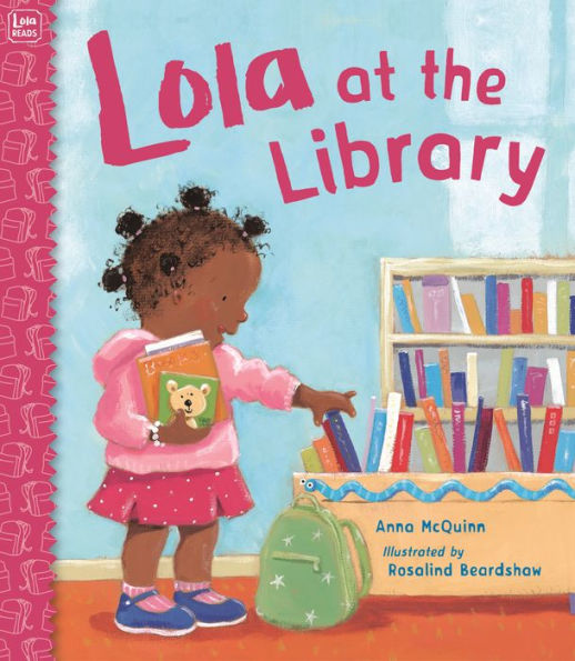 Book cover of "Lola at the Library" by Anna McQuinn shows a young girl with curly hair reaching for a book. She's holding a teddy bear book, wearing a pink outfit, and standing by a book display.