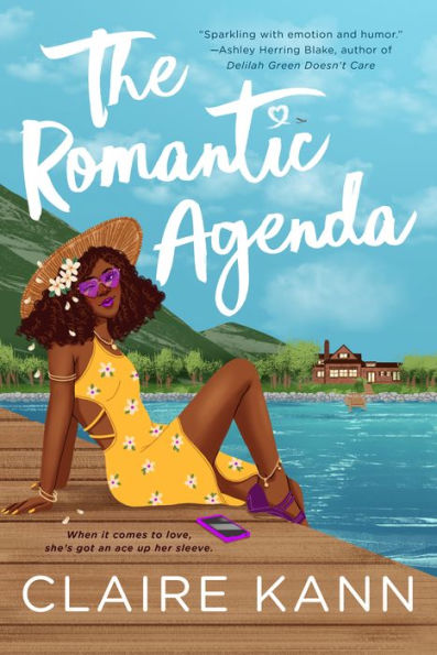 Book cover of "The Romantic Agenda" by Claire Kann. A woman in a yellow floral dress relaxes on a dock by a lake, wearing purple sunglasses. The scene is sunny with a house across the water.