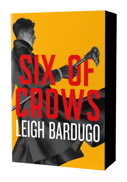 Deluxe edition cover of “Six of Crows” by Leigh Bardugo. The design features bold red title text against a bright yellow background, with a black-and-white illustration of a man in a long coat holding a staff or cane.