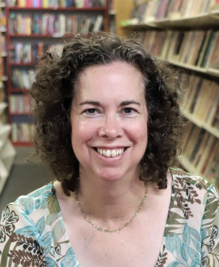 Author, Maria V. Snyder, wearing a green-blue floral designed shirt, with a skinny, green necklace, smiles while looking forward.