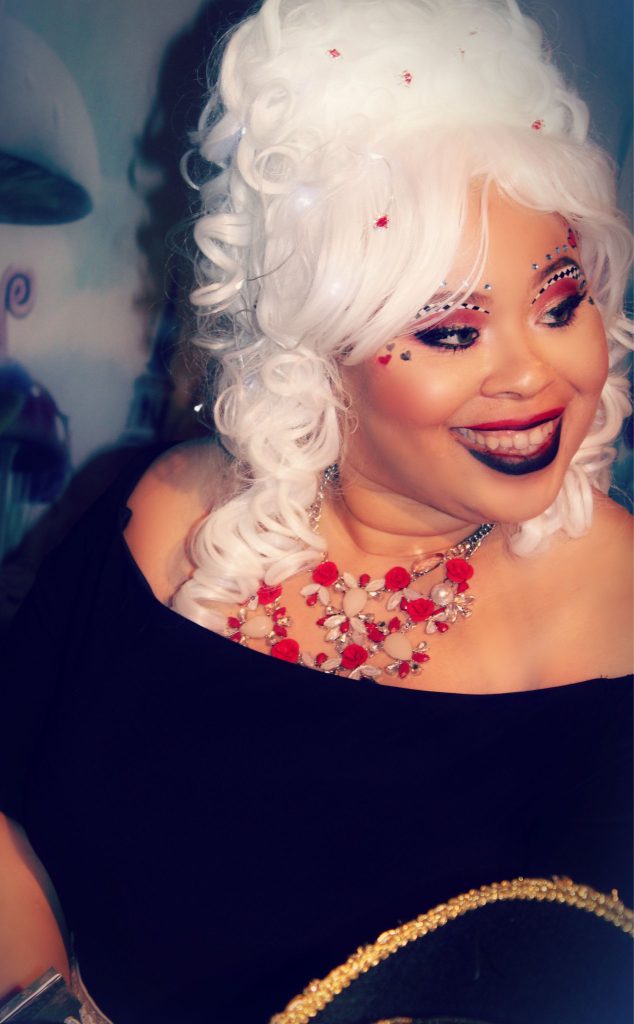 Author L.L. McKinney, an African American woman, wearing a black off-shoulder top, with a red-pink floral necklace, smiling and looking to the side.