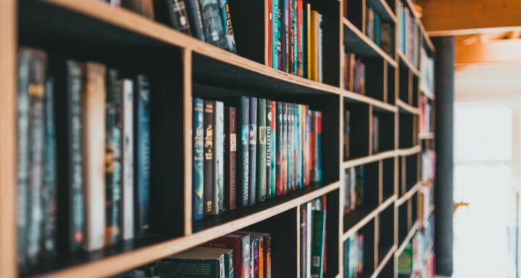 Depicts a library shelf very close to the camera with many book spines in view.