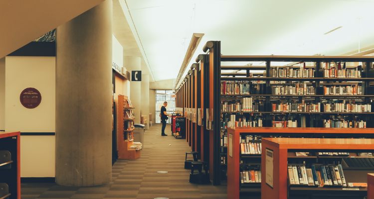 Depicts a hallway within a library with many aisles to the right and a staircase to the left.