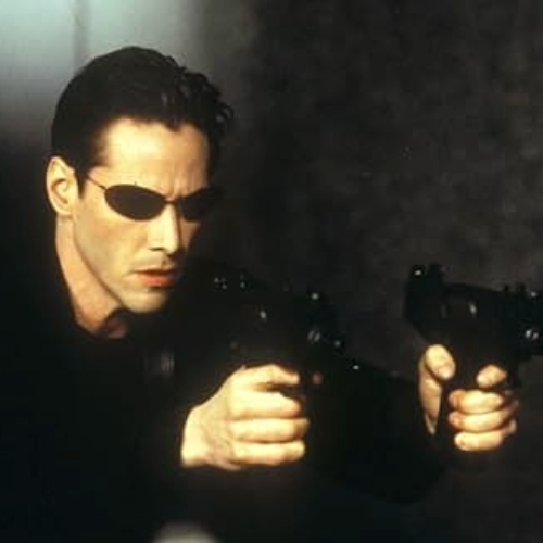 Movie still of Keanu Reeves holding two guns, starring in The Matrix.