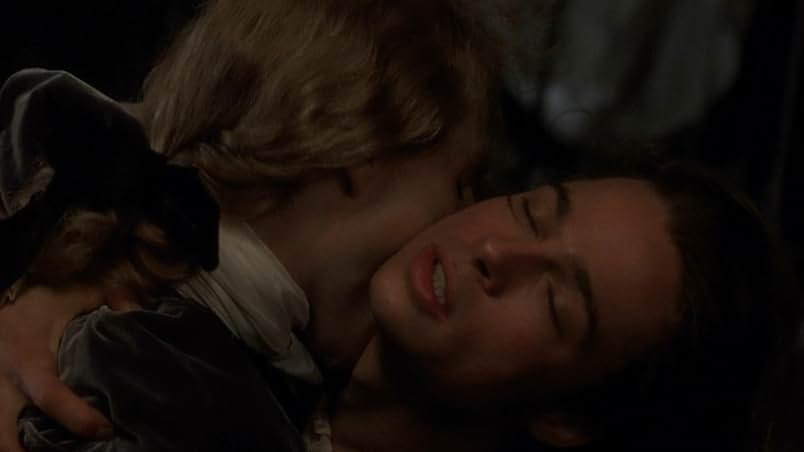 A still from the 1994 film Interview with the Vampire. A man leans back with his eyes closed while a vampire with long blonde hair tied in a brown ribbon and wearing 18th Century clothing bites into the man's neck.