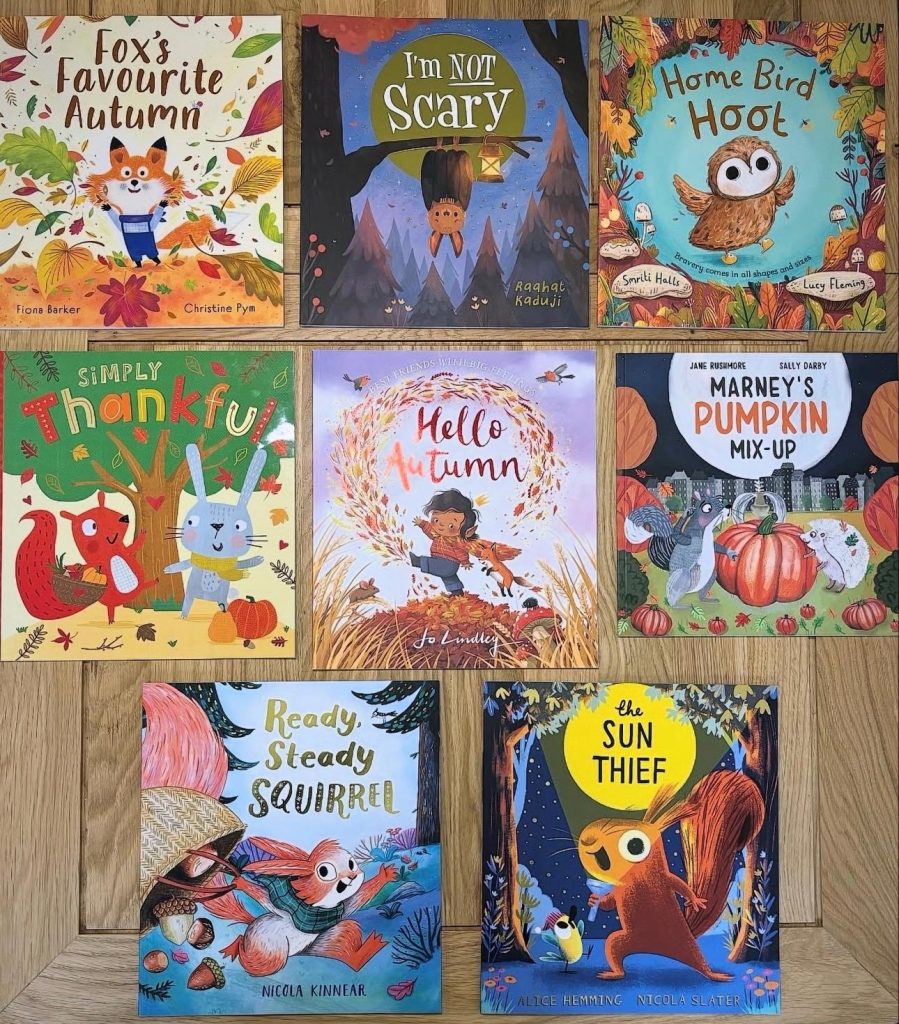 Eight Autumn themed children's book laid out on a wooden table in three rows, three books in the first two rows and two books in the bottom row. The titles include: Fox's Favorite Autumn, I'm Not Scary, Home Bird Hoot, Simply Thankful, Hello Autumn, Marney's Pumpkin Mix-Up, Ready, Steady Squirrel, and The Sun Thief.