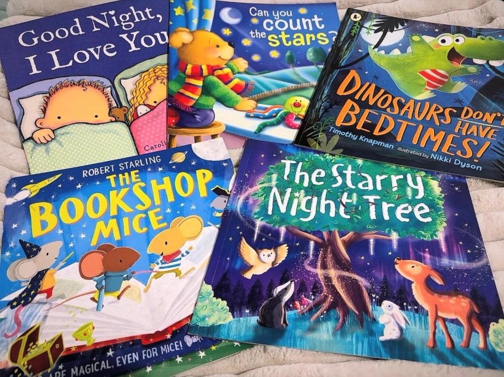 On top of a cozy blanket are five picture books for young children complete with furry woodland creatures, dinosaurs, and little kids tucked in bed. Featured titles are: Good Night, I Love You, Can You Count The Stars?, Dinosaur Bedtime, The Bookshop Mice, and The Starry Night Tree.