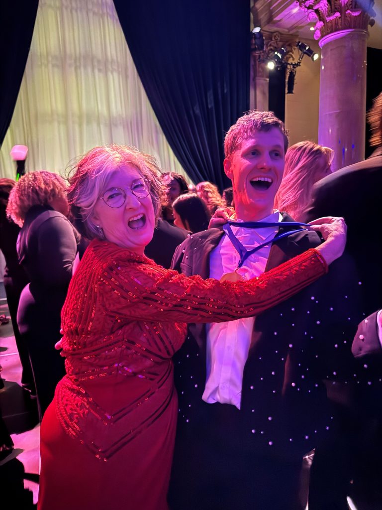 Christopher at the National Book Awards wearing a big smile on the dance floor as Barbara Kingsolver, in a stunning red, sequined dress, puts her Lifetime Achievement Award around Christopher's neck.