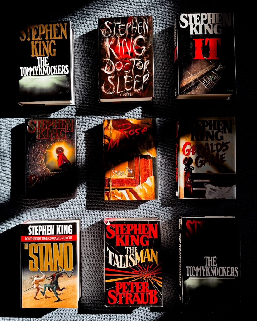 Depicts dark and shadowy photo of nine Stephen King books laid out in a 3 by 3 row.
