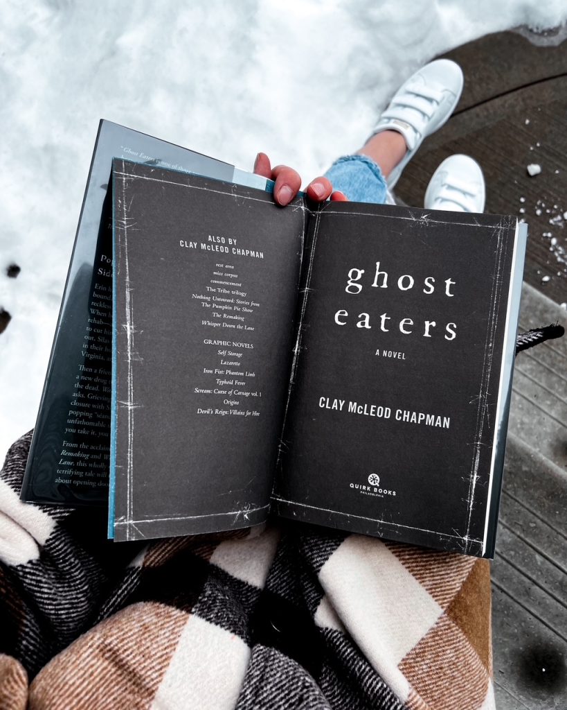 Depicts photo of Ghost Eaters by Clay McLeod Chapman, sitting opened to the title page on someone's lap.