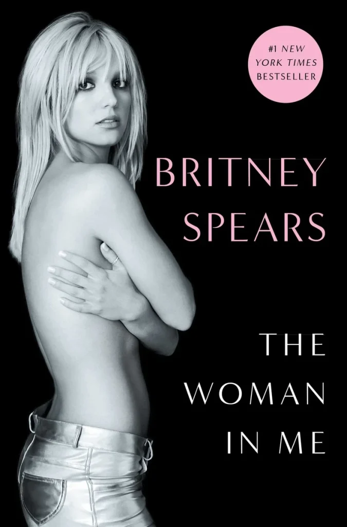 The Woman in Me, a memoir by pop star Britney Spears book cover. Depicts black background against pink text and a black and white cut out of Britney Spears, topless covering her chest with her arms.