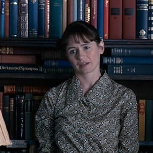A woman leans against a bookshelf looking confused.