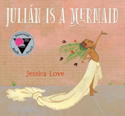 "Julián Is a Mermaid" by Jessica Love, a children’s book cover showing a child in a cream-colored mermaid costume striking a joyful pose against a brick wall with a crown of green leaves.