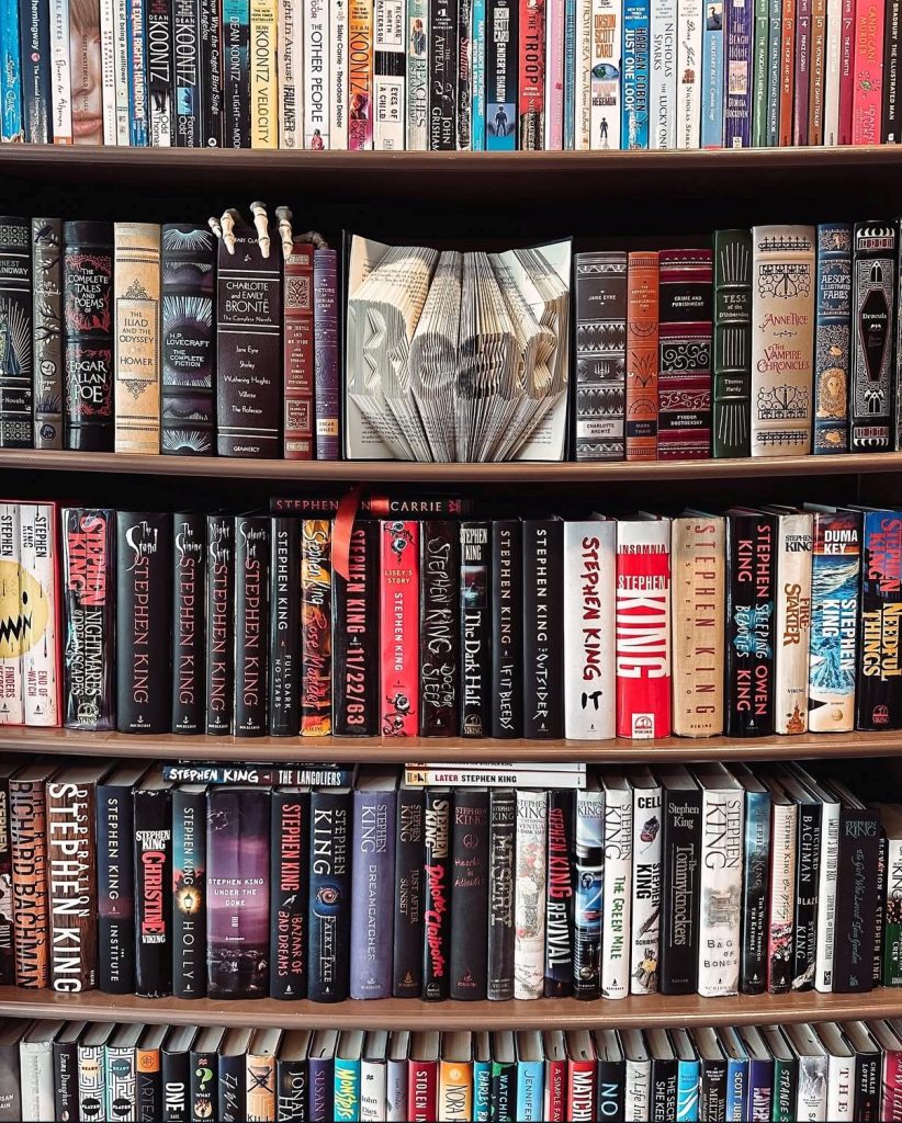 Bookstagrammer Laura's bookshelf shows two full shelf rows of exclusively Stephen King novels. On the first book shelf Laura shows her classics collection on both sides of a 3-D art piece carving of a book's pages that looks like the word "Read."