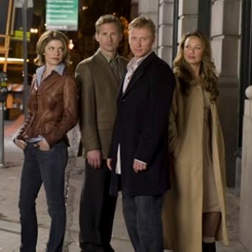 The original cast of Journeyman, wearing long coats, stood in a formation on the street at night time.