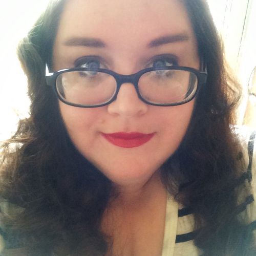 Author, T.A. Teufel, wearing a black-white stripy top and black framed glasses, smiling and looking ahead.