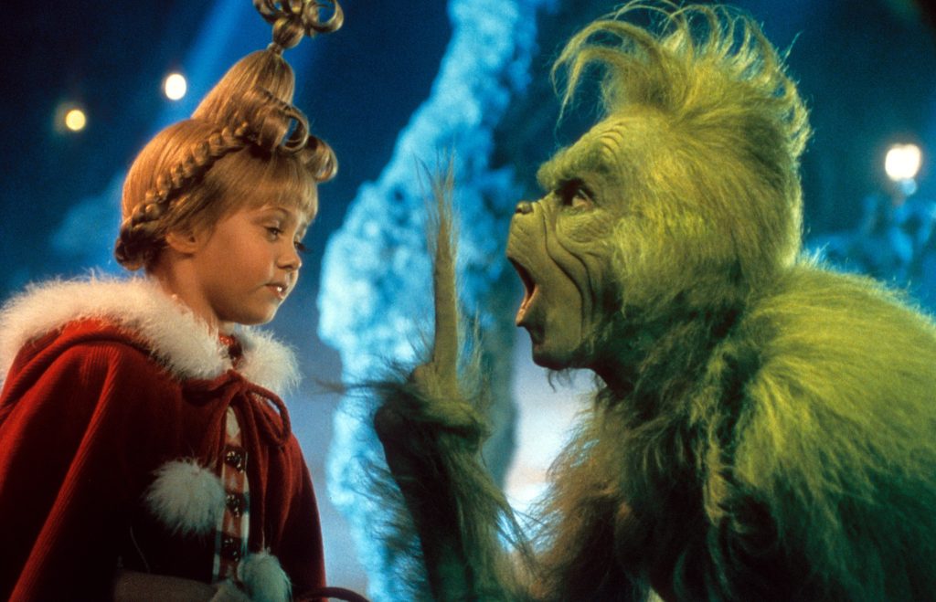 Still from How the Grinch Stole Christmas depicting the Grinch (Jim Carrey), a furry green creature, speaking to Cindy Lou Who (Taylor Momsen), a young girl with a blonde updo and red coat.