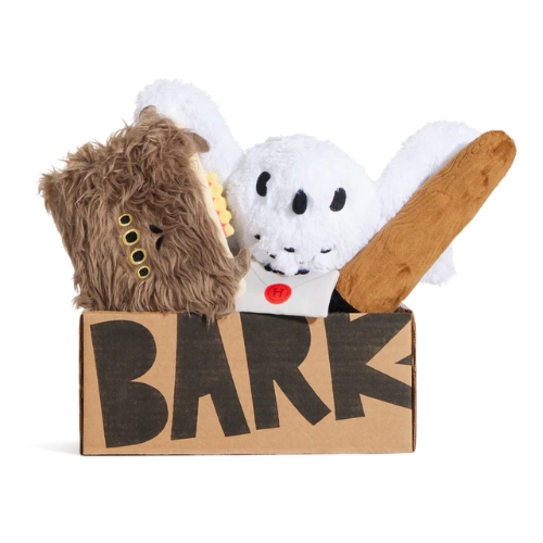 A cardboard box labeled "BARK" contains three plush toys: a furry brown creature, a white owl, and a bat.