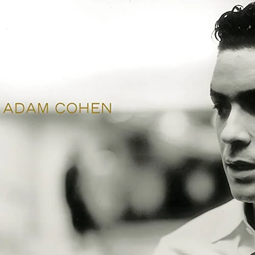 The album cover for Adam Cohen's debut record. A black and white photograph of part of Adam Cohen's face with the background blurred. He has pale skin and dark hair. His name is left-aligned in the center in golden text.
